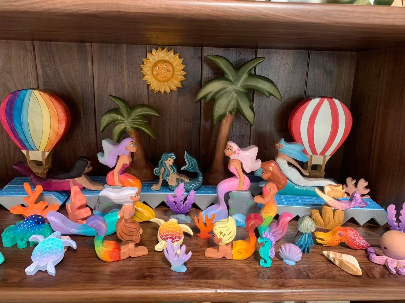 Scene of wooden toys featuring mermaids, and sea creatures by the ocean side in an array of colors